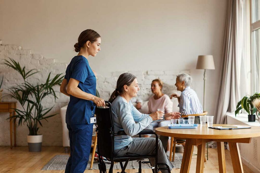 Older adult and family member organize labeled clothing, toiletries, photos, and a walker in an assisted living room.