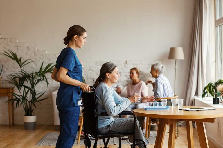 Older adult and family member organize labeled clothing, toiletries, photos, and a walker in an assisted living room.